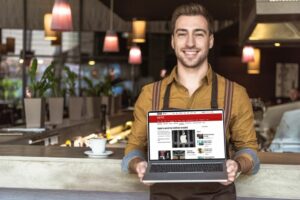 handsome young man holding a laptop which is showing his small business website